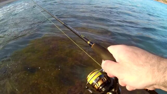 POV of angler with bent rod as fish splashes on water surface during shore fishing