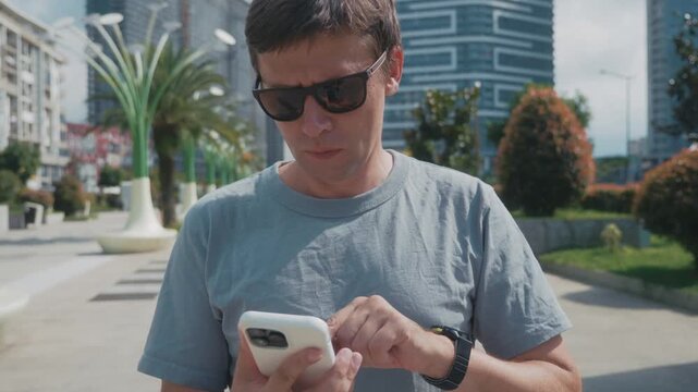 Man monitoring workout recovery and heart rate on smartwatch, checking training results in smartphone fitness app while standing in urban park.