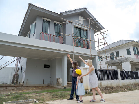 Family consist father mother daughter visit new construction two-story house. pointing at different part building expressing excitement anticipation for their future home. indicat ongoing construction