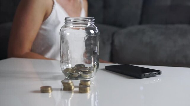 Static shot of a woman taking paper money out of a glass jar, demonstrating spending savings, cash withdrawal, or emergency expenses.
