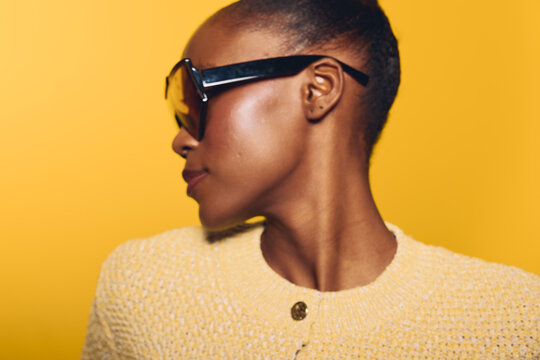 Profile of a dark skinned African woman wearing sunglasses and a yellow textured sweater against a bright yellow background. Concept of fashion, style, and confident beauty.