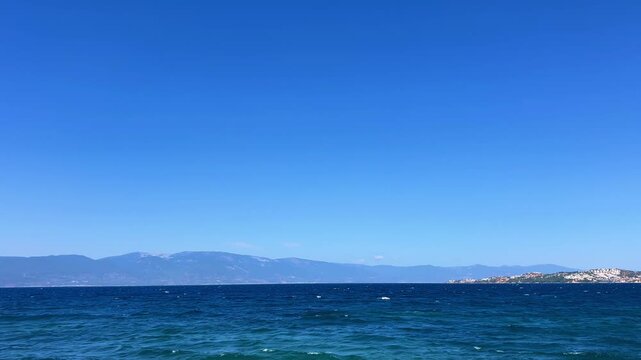 Deep cobalt Aegean waters showing whitecaps and ripples under a clear cloudless sky with distant mountain ranges along Ayvalik coast.