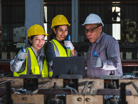 Diverse Industrial Engineer Collaborating with Laptop in Steel Factory: Multiethnic team hardhat discussing technical data and coil inventory ideal smart manufacturing teamwork concept.