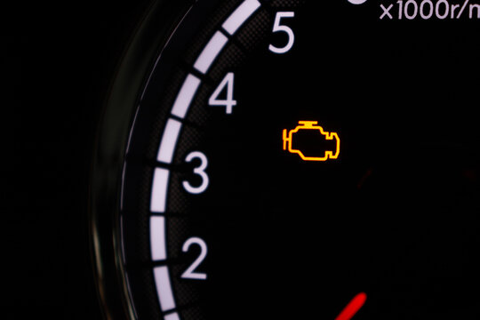 Close-up of car dashboard showing check engine light warning icon on rpm gauge.