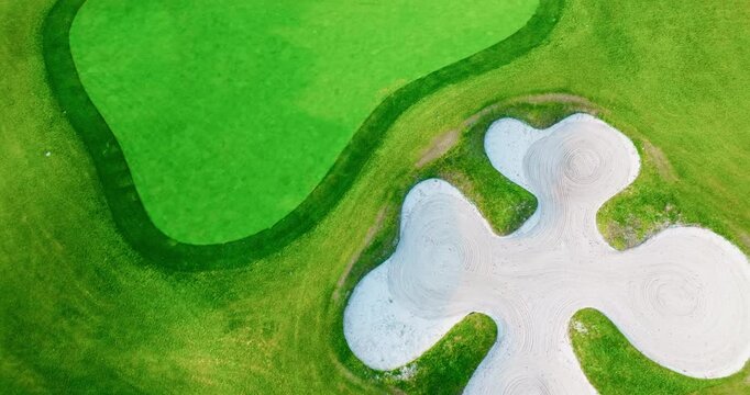 Top aerial view of a cross-shaped sand bunker on a green golf course fairway under bright natural daylight.
