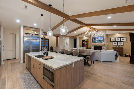 Open concept kitchen island with marble countertops, rustic wooden beams, warm pendant lighting beam