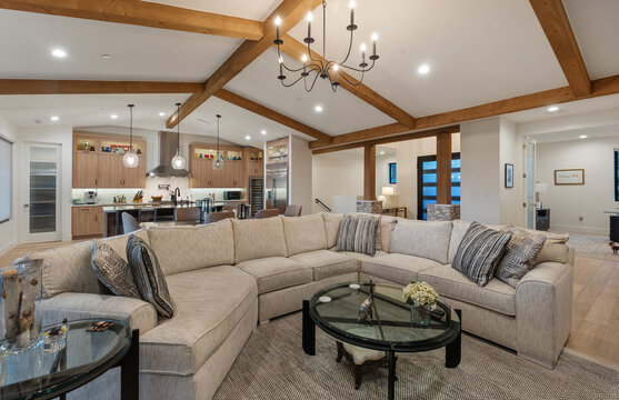 Open plan living room kitchen with wooden beams and chandelier lighting over sofa seating zone charm