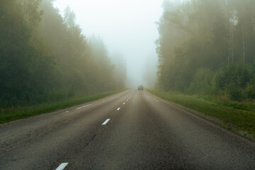 Police patrol car disappearing into morning fog on a forest road © Edijs