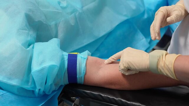 Medical professional wearing sterile gloves palpating a vein on a patient's arm before an injection or blood test, with a tourniquet applied to make the vein more prominent