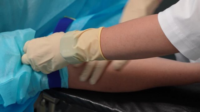 Medical professional wearing sterile gloves palpating a patient's arm to find a vein after applying a tourniquet, preparing the area for an intravenous injection or a blood test procedure