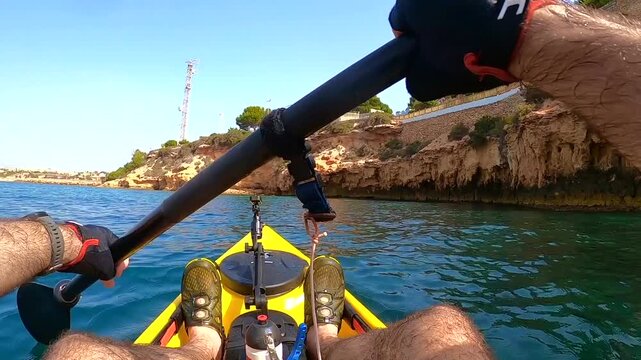 First person point of view paddling kayak along Mediterranean cliff and sea promenade