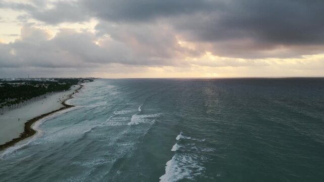 Aerial view of gentle waves rolling toward a coastline at twilight