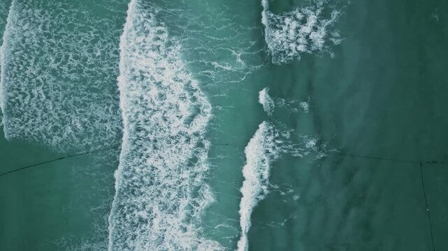 Aerial view of rippling teal waves breaking in rhythmic white foam