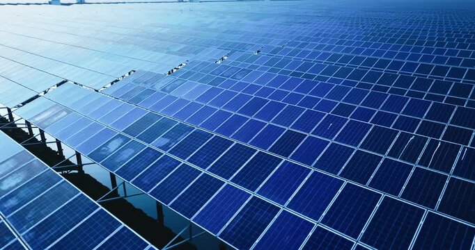 High angle view of a vast solar panel farm array under bright daytime lighting, showcasing neat geometric blue panels.