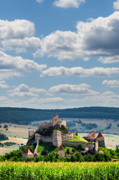 Rupea Fortress medieval citadel rising above rolling green countryside and cornfields under dramatic cloudy sky, Rupea, Transylvania, Romania