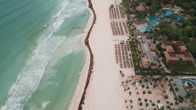 Aerial view of a curving resort shoreline with turquoise surf and patchy sargassum