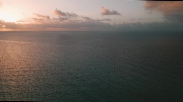 Aerial view of open ocean water glowing under a soft golden sunset