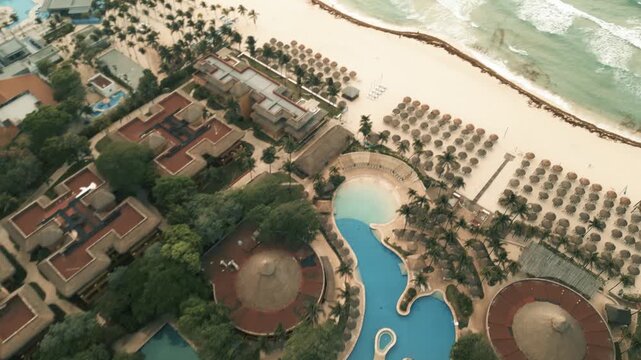 Aerial drift over a beachfront resort with curving pools and shoreline