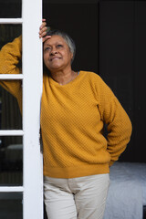 Naklejka premium Senior African American woman leaning on white door at bedroom doorway in mustard sweater