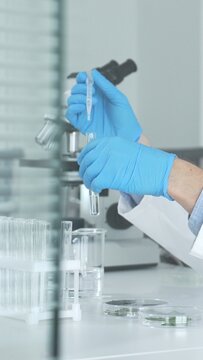 Biologist or chemist performing precise liquid handling with a micropipette into a clear glass beaker