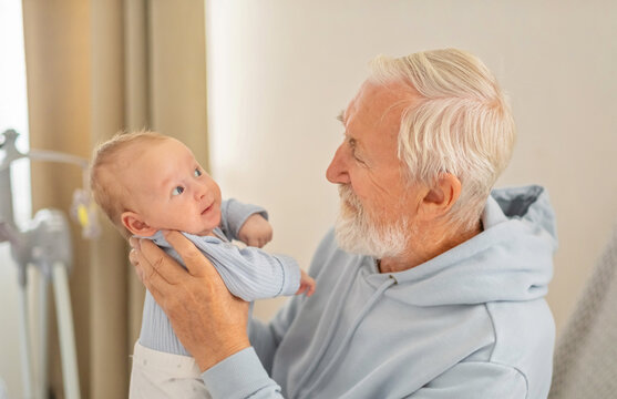 Elderly man smiles at baby who watches him with attention, contact through eyes and quiet voice, emotion impossible to stage. Close-up shot. Concept of eye contact between grandfather and baby