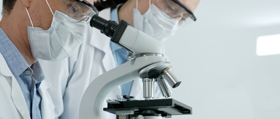 Scientists focus at a microscope in a bright laboratory, performing medical research and...