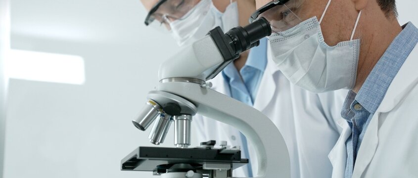 Scientists focus at a microscope in a bright laboratory, performing medical research and contributing to advancements in science, health, and biomedical technology
