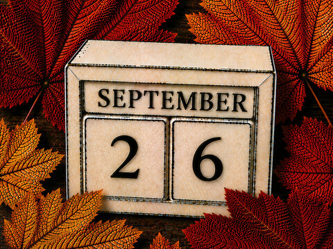 Wooden block calendar showing September 26 date surrounded by colorful autumn maple leaves on dark background