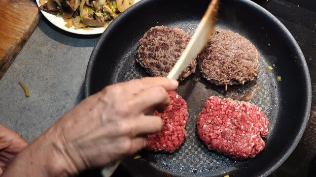 Stockholm, Sweden A cook in a residential kitchen fries homemade hamburger patties in a frying pan. 