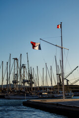 Fototapeta premium Large French national flag waving on a mast at a harbor shipyard