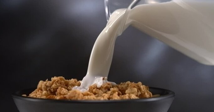 Milk pouring onto granola in bowl for breakfast in slow motion close up