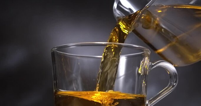 Tea pouring from glass teapot into transparent cup in slow motion