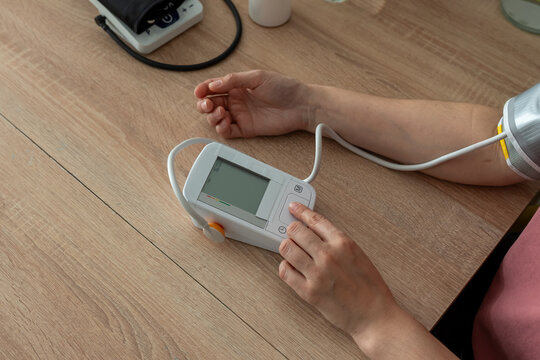 Overhead close up of a woman pressing the button on a digital blood pressure monitor with a cuff around her arm at home. Concept of self monitoring, home healthcare and preventive health habits.