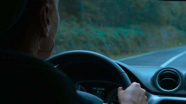 Woman drives a modern car along a picturesque countryside road, gripping the steering wheel as lush forests and beautiful nature glide by, creating a sense of freedom and adventure