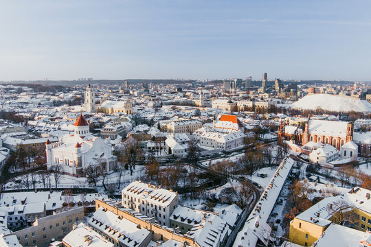 Aerial winter view of the Bernardine Church in Vilnius, Lithuania, with Gediminas Castle Tower and the Three Crosses Monument. Snowy cityscape in warm afternoon light.