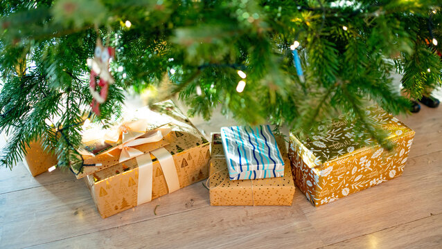 Wrapped Christmas gifts arranged under a decorated evergreen tree at home. Festive presents, warm lights and natural fir branches create a cozy holiday atmosphere.