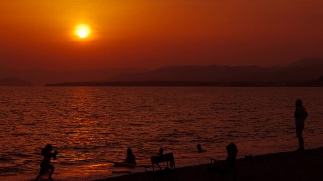 Teenagers beach vacation in nightfall. Happy teenagers silhouettes pass free time on the seashore during dusk time. A concept of happy vacation time in summer