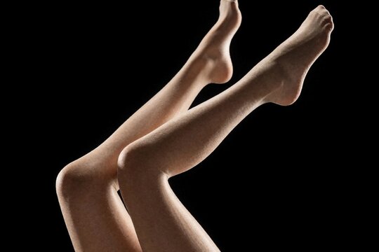 Slender female legs in pantyhose pose on black backdrop. Elegant nylon stockings emphasize graceful shape. This image suits fashion, beauty, and style content.