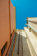 Metal fire escape ladder on a brick wall between buildings close up. This is a narrow urban street alley. Industrial architecture exterior on a bright sunny day. Clear blue sky backdrop.  © Dmitry Presnyakov