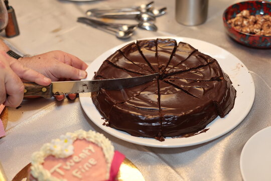 Personne d&eacute;coupant un g&acirc;teau au chocolat recouvert de ganache