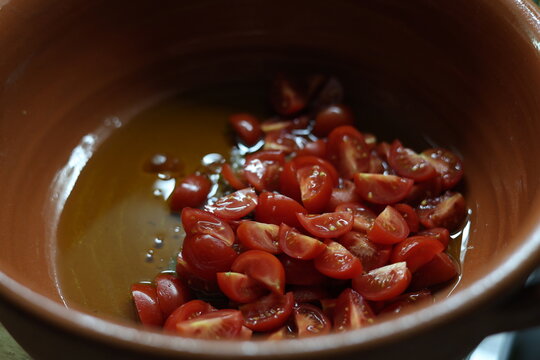 Tomates cerises coup&eacute;es dans un plat en terre cuite avec huile d'olive