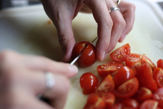 Mains coupant des tomates cerises fra&icirc;ches au couteau sur une planche