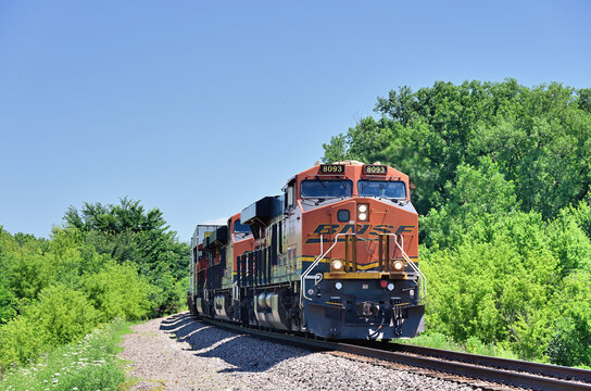 A single locomotive powers a westbound Burlington Northern Santa Fe container train as it negotiates a curve while emerging from a tree-lined right-of-way in north central Illinois.. 