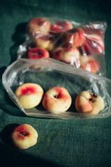Say no to plastic packaging concept, fresh organic saturn peaches trapped inside a disposable cellophane bag, environmental pollution and single use plastic waste issue © sloona