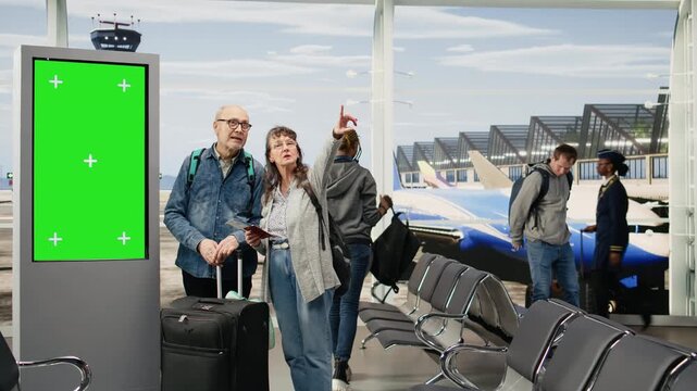 Chroma key departure board stands beside an elderly couple in an airport terminal as they plan an itinerary and travel agenda, reflecting an unconventional retirement lifestyle and world travel.