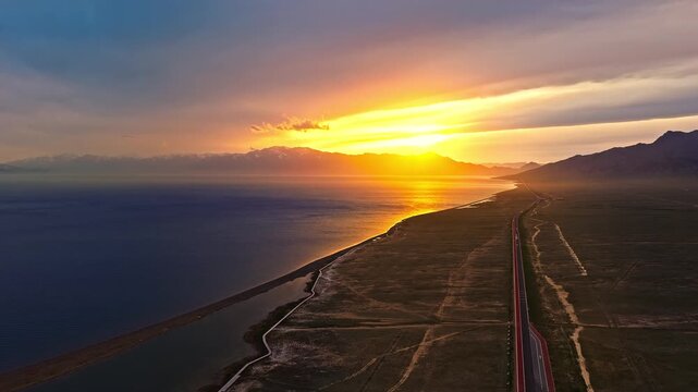 Aerial drone view of golden hour sunset over tranquil lake and scenic road at Sayram Lake, Xinjiang, China