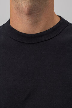 Close-up macro shot of a man's neck wearing a plain black crew-neck t-shirt. Focus on the ribbed collar, stitching detail, and cotton fabric texture. Perfect for clothing mockup.