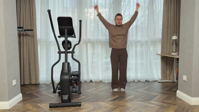 Woman in warm casual home clothes performs circular shoulder movements forward and backward. Simple indoor warmup for joints and posture.