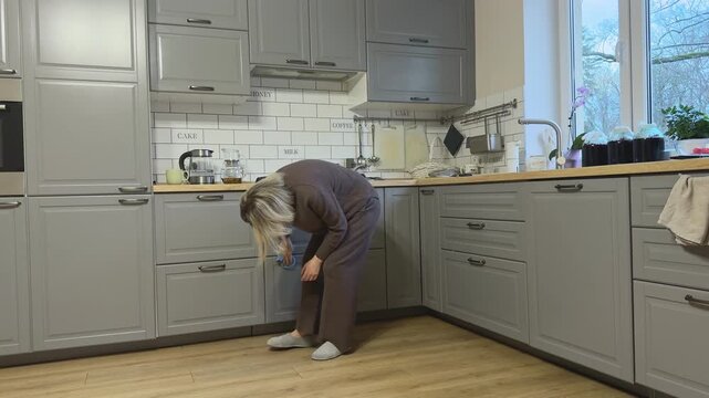Female wipes lower cabinet fronts maintaining kitchen cleanliness.