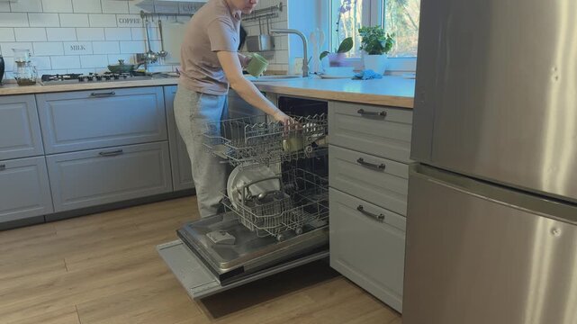 Cups taken from sink and placed into dishwasher during daily kitchen cleaning routine.